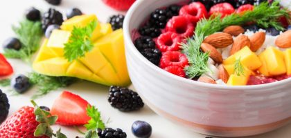 A vibrant bowl filled with fresh berries, mango, almonds, and herbs, perfect for a healthy snack or breakfast.
