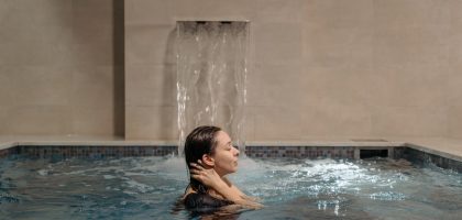 Adult woman relaxing in an indoor swimming pool near a cascading waterfall.