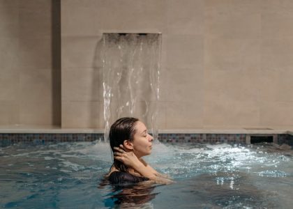 Adult woman relaxing in an indoor swimming pool near a cascading waterfall.