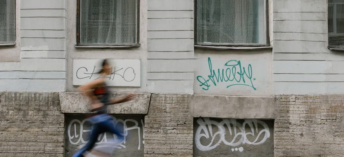 Blurred motion of a woman running past a graffiti-covered urban wall. Captures dynamic energy.