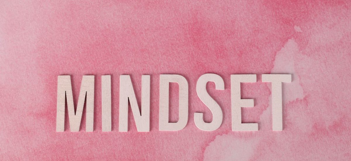 Wooden letters spelling 'MINDSET' on a textured pink background, symbolizing motivation.