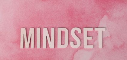 Wooden letters spelling 'MINDSET' on a textured pink background, symbolizing motivation.